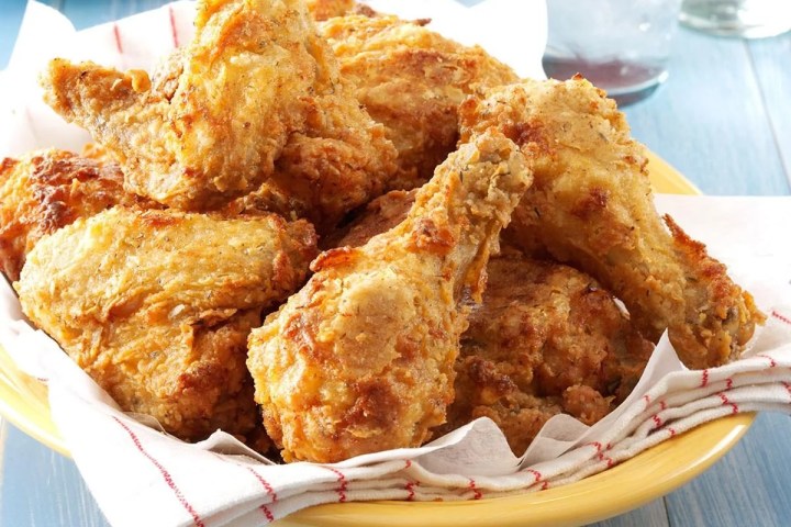 Plate of crispy fried chicken drumsticks with napkin on wooden table.