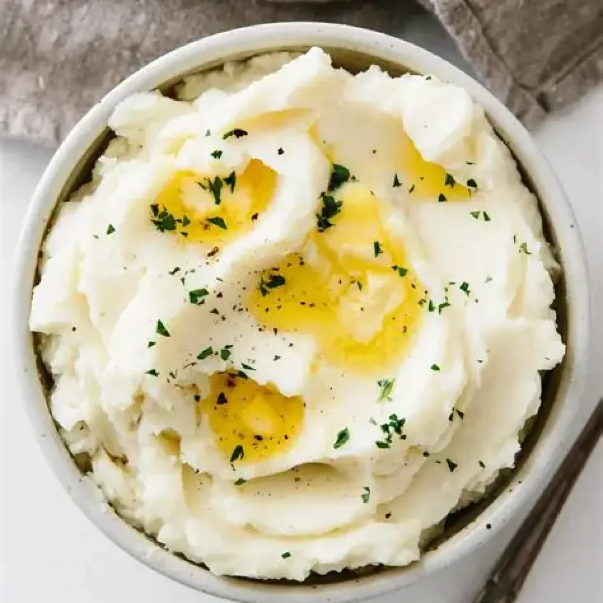 Bowl of mashed potatoes with butter and parsley garnish on top.