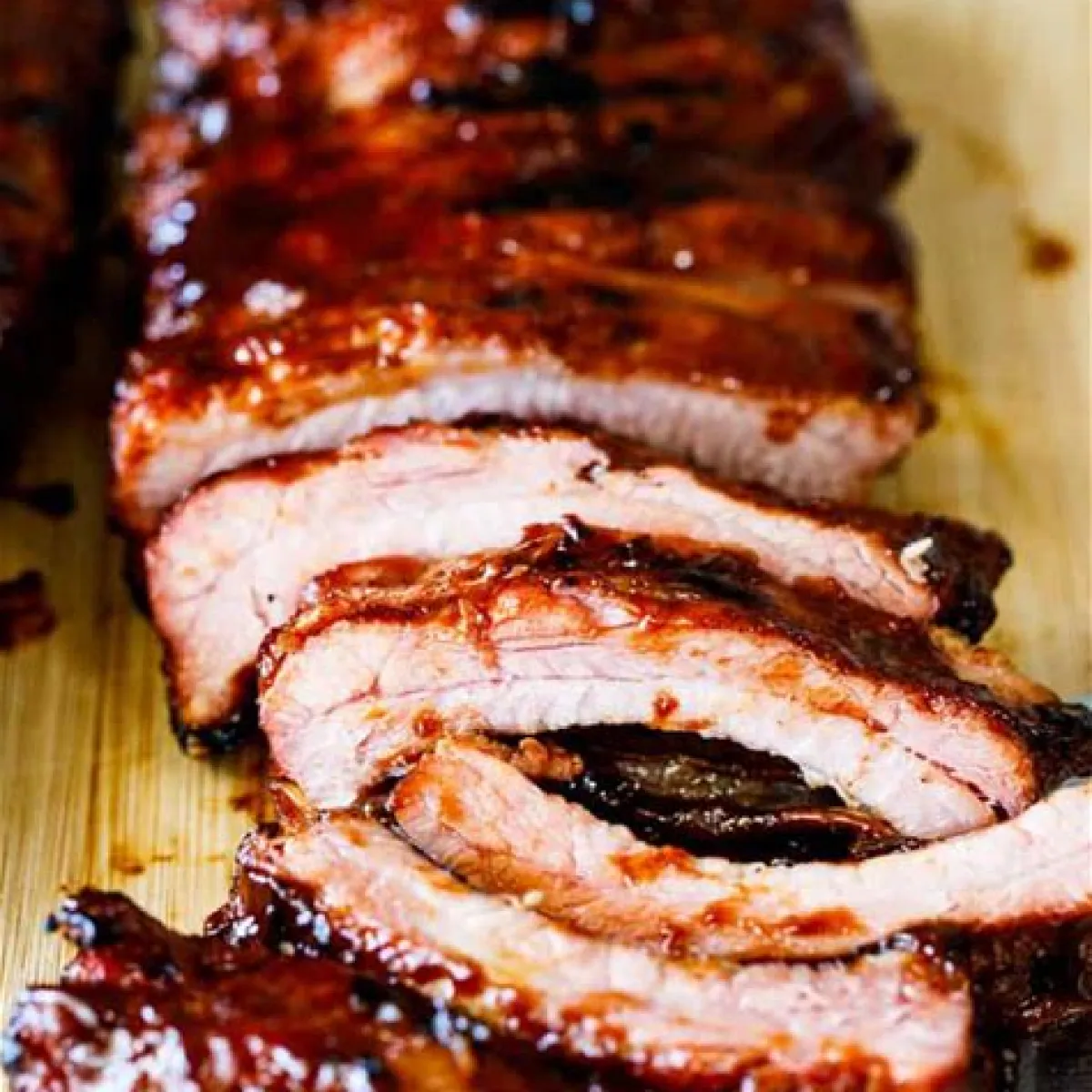 Sliced barbecued ribs on a wooden cutting board.