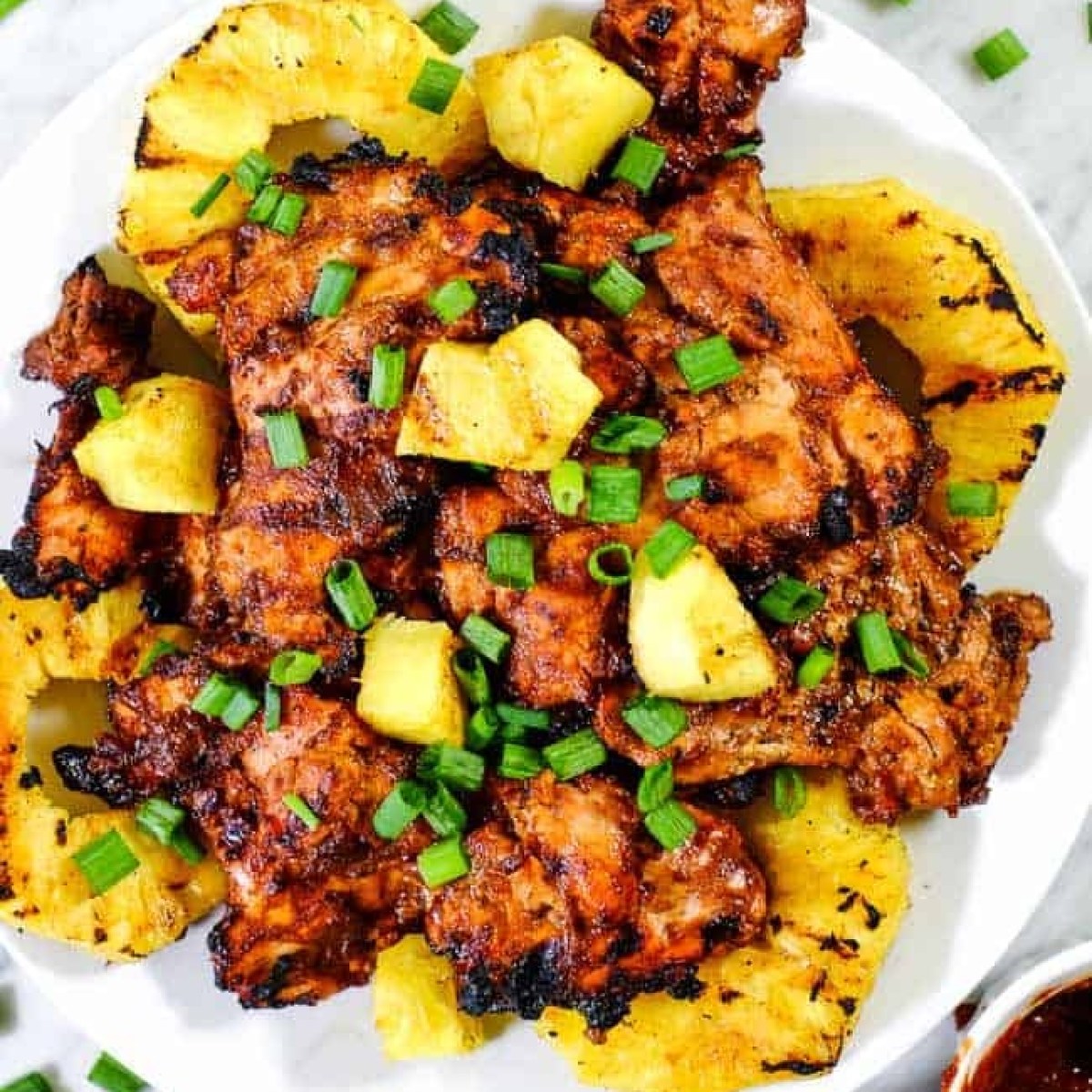 Grilled meat and pineapple slices garnished with green onions on a white plate.