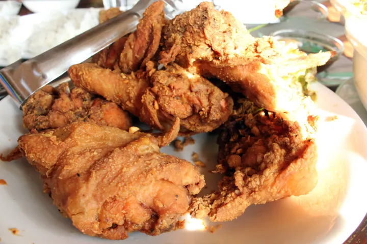 Plate of crispy fried chicken pieces with metal tongs.