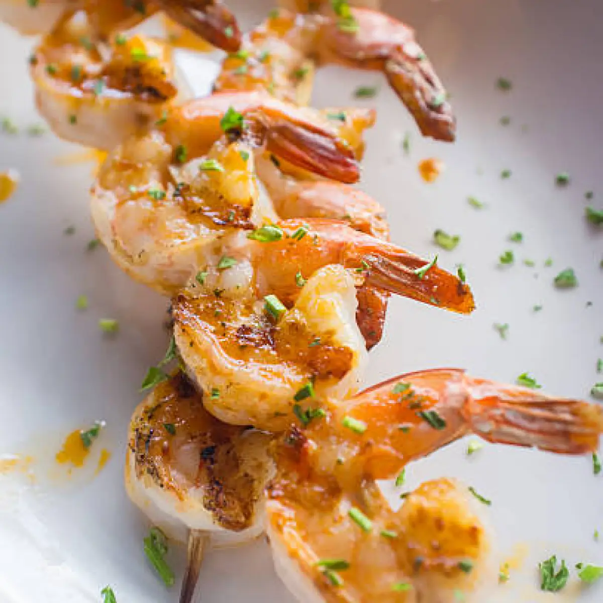Grilled shrimp skewers garnished with herbs on a white plate.