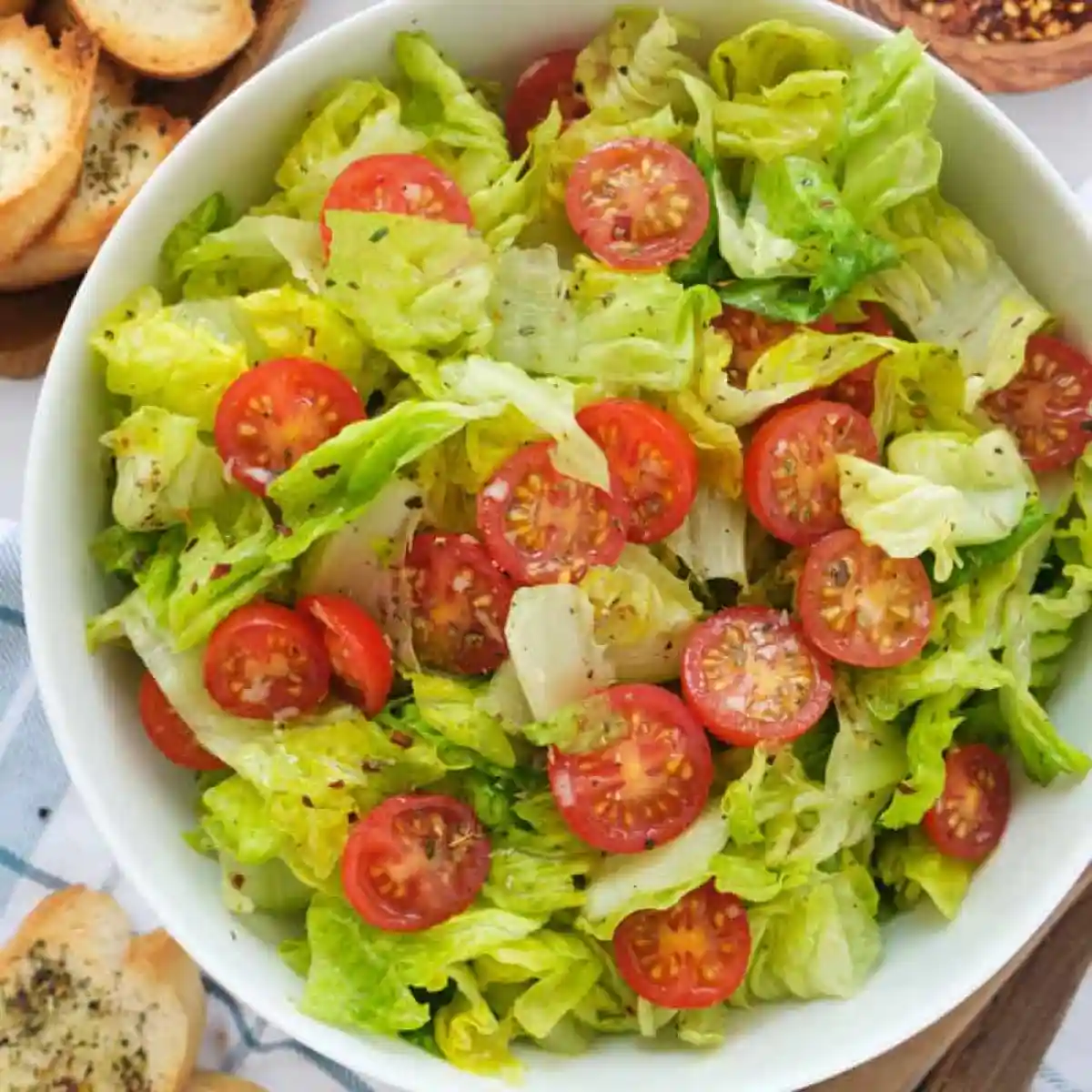 Bowl of salad with lettuce and cherry tomatoes next to garlic bread slices.
