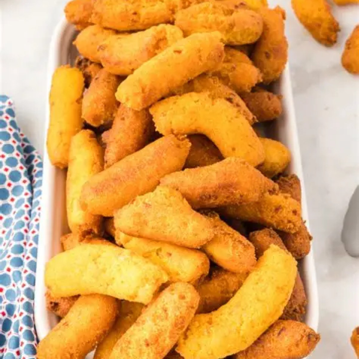 A platter of golden, crispy fried corn sticks on a table with a patterned cloth.