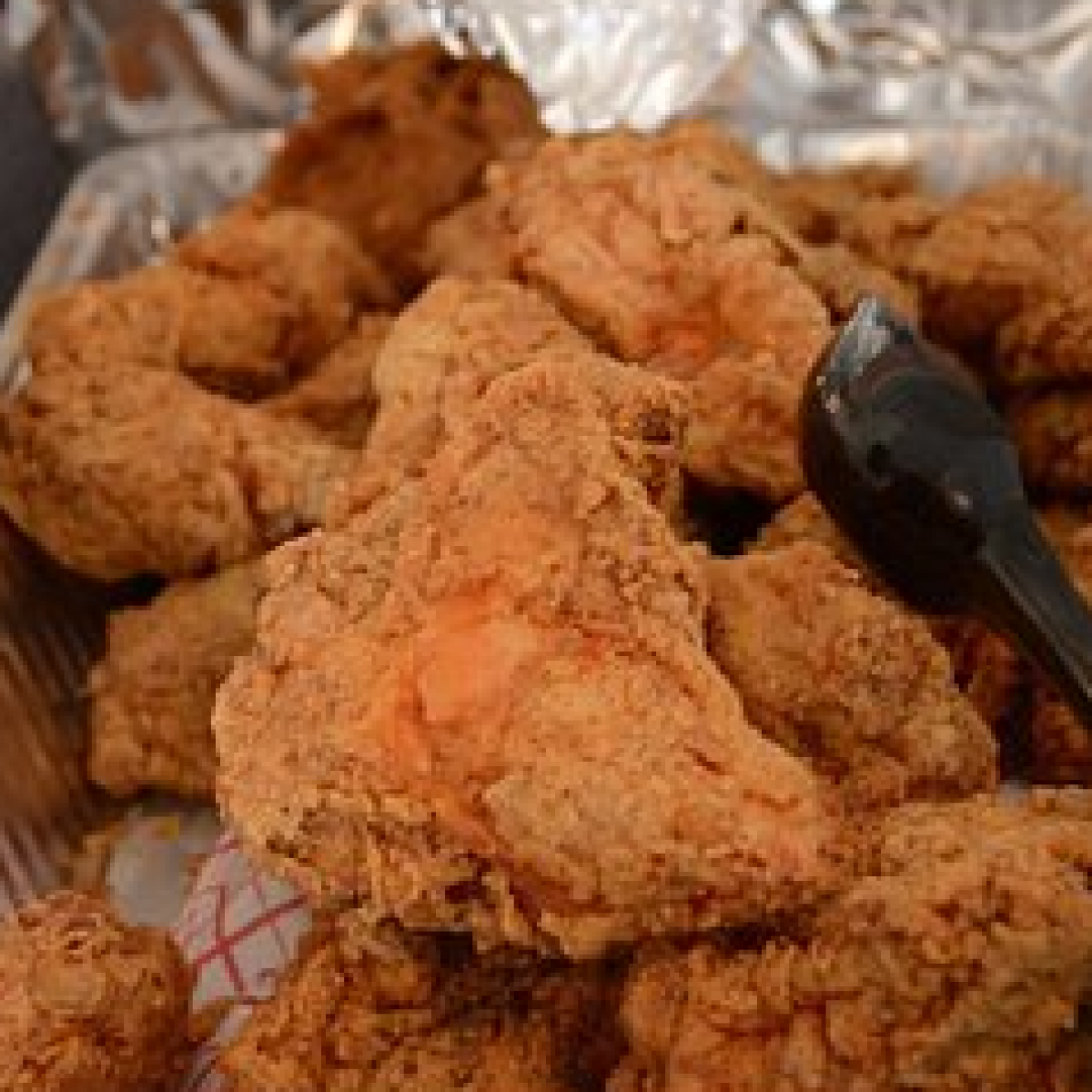 Tray of fried chicken pieces with black tongs.