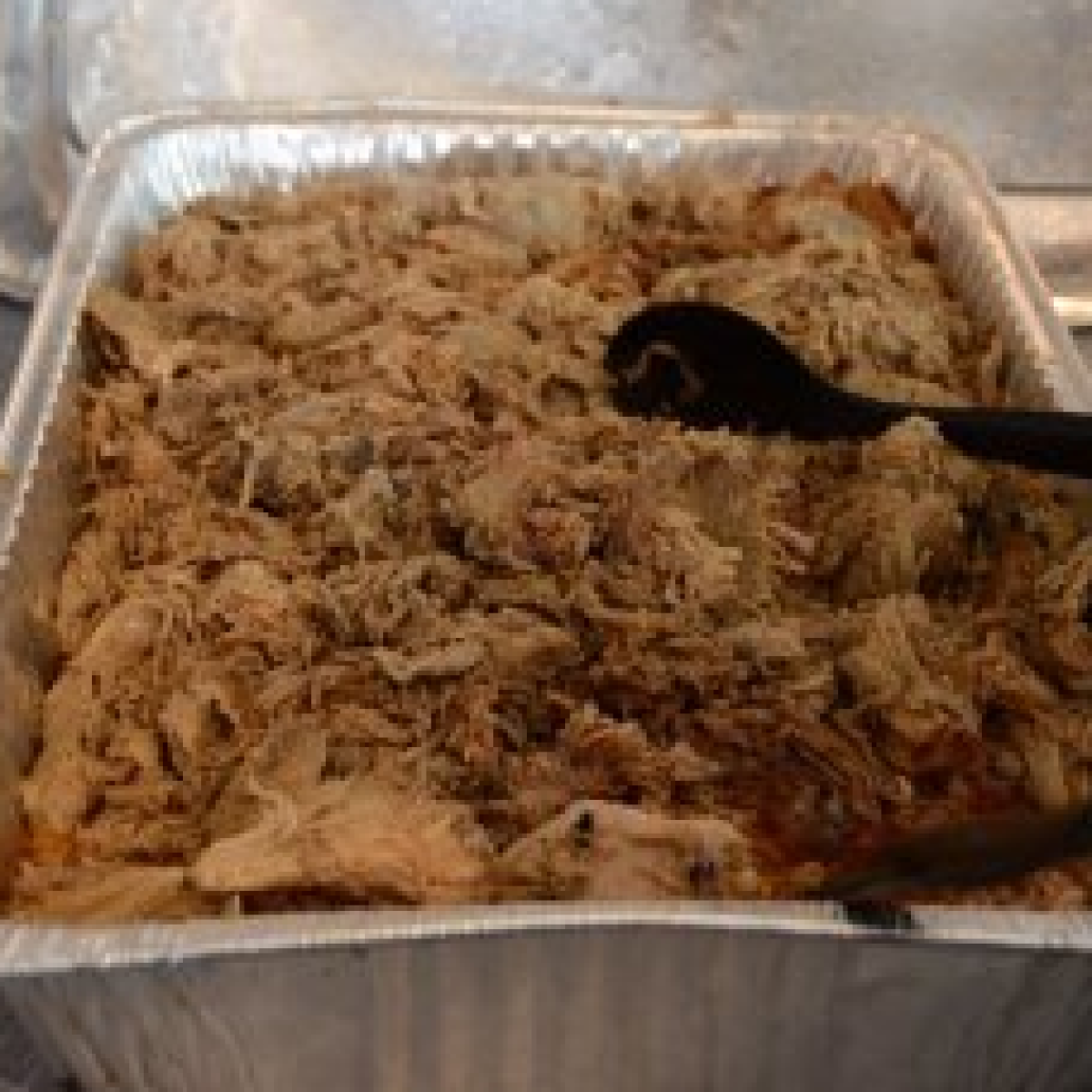 Tray of shredded brown meat with tongs on top.