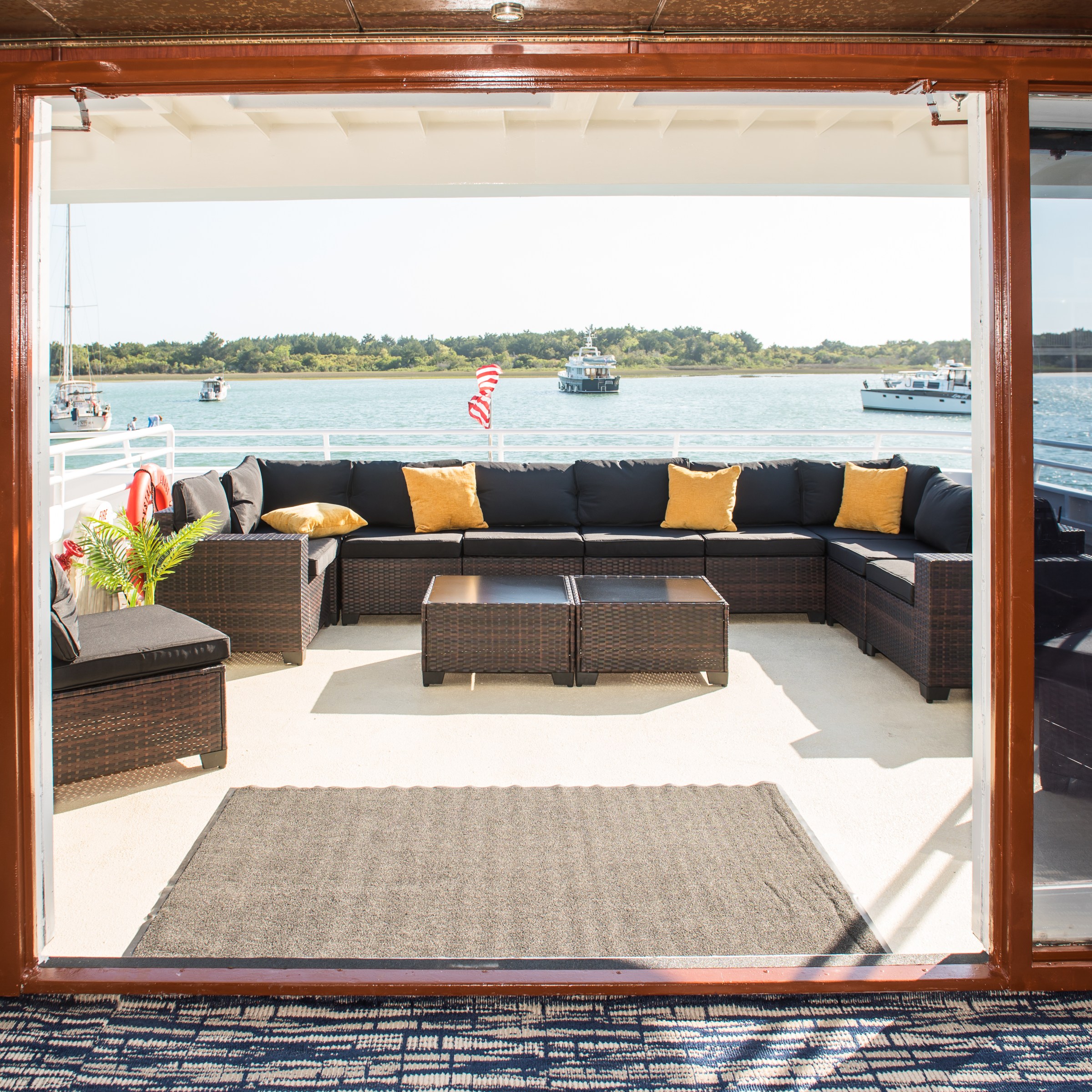 Yacht deck with black wicker furniture, yellow cushions, overlooking a calm sea.