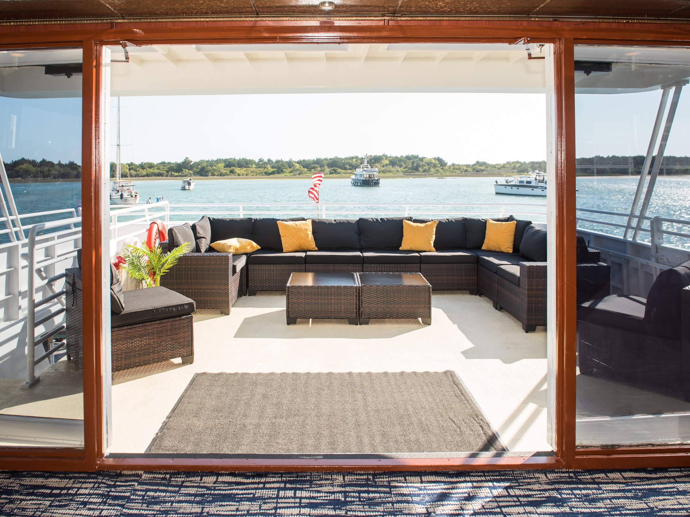 Yacht deck with black wicker furniture, yellow cushions, overlooking a calm sea.