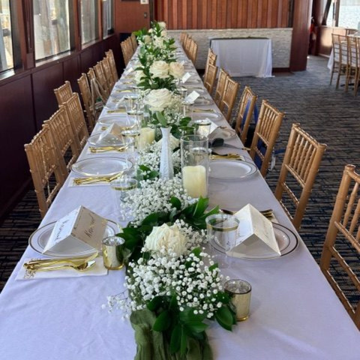 Elegant banquet table with white flowers, candles, and gold chairs on a boat.