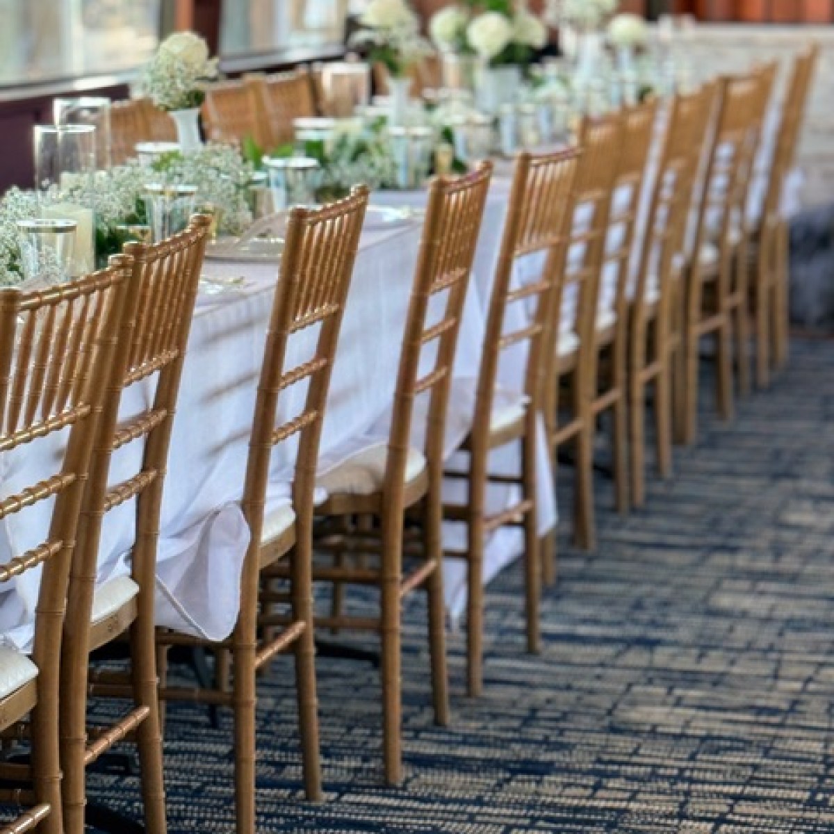 Elegant long dining table set with white cloth, gold chairs, and floral centerpieces.