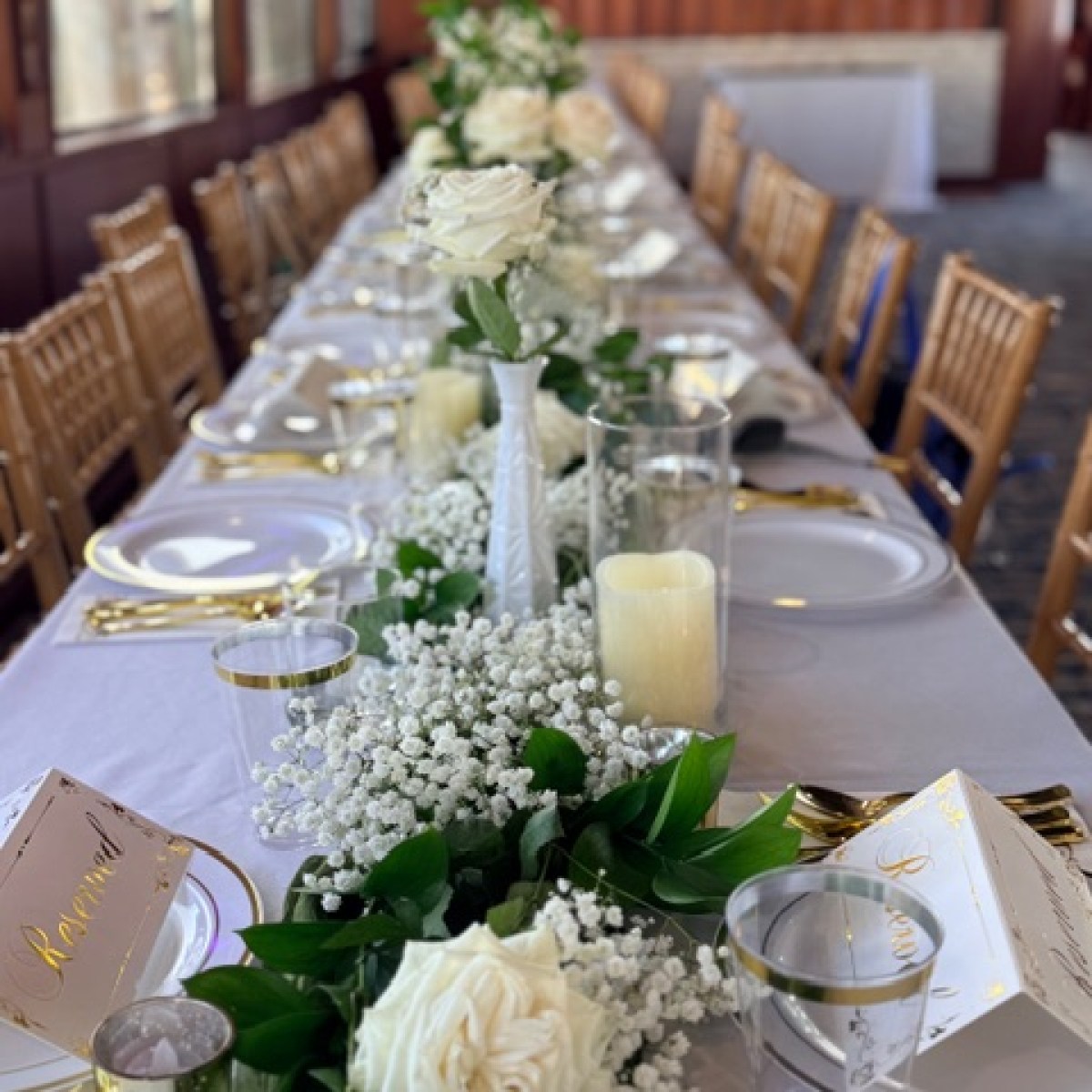 Elegant dining table with white roses, greenery, candles, and gold accents in a classy setting.