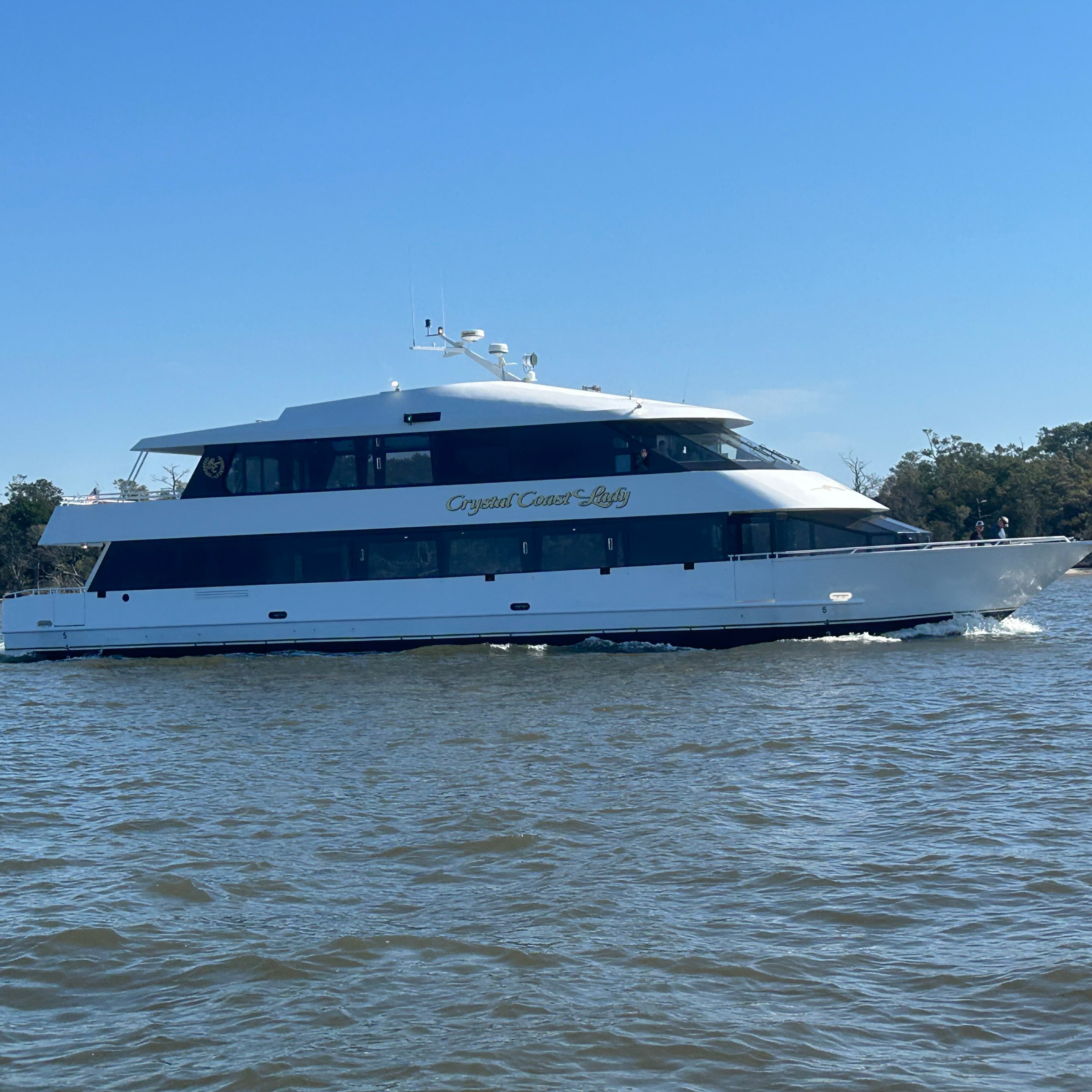 White yacht cruising on a river with trees in the background under a clear blue sky.