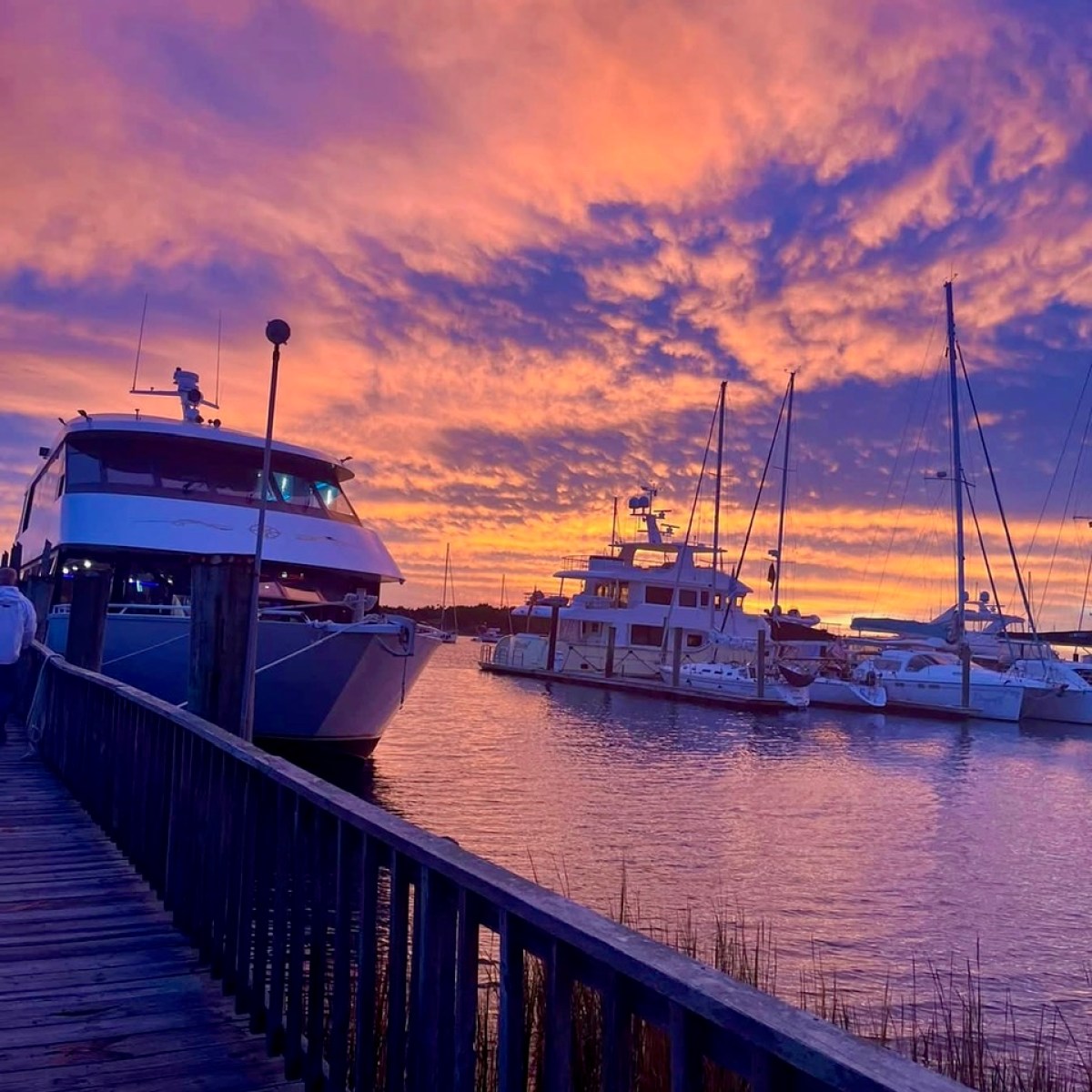 Boats docked at a marina under a vibrant orange and purple sunset sky.