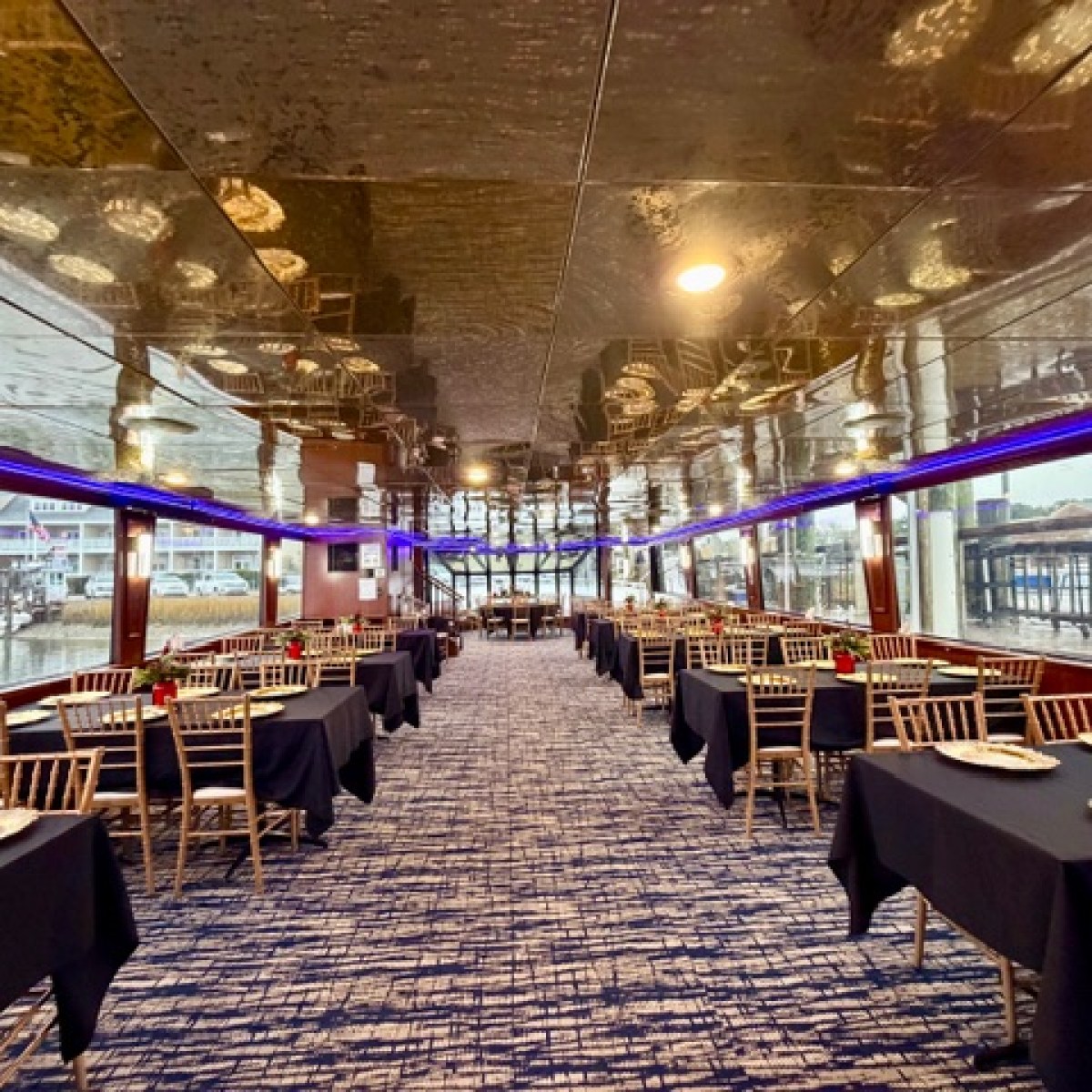 Elegant boat dining area with tables set for an event, featuring large windows and mirrored ceilings.