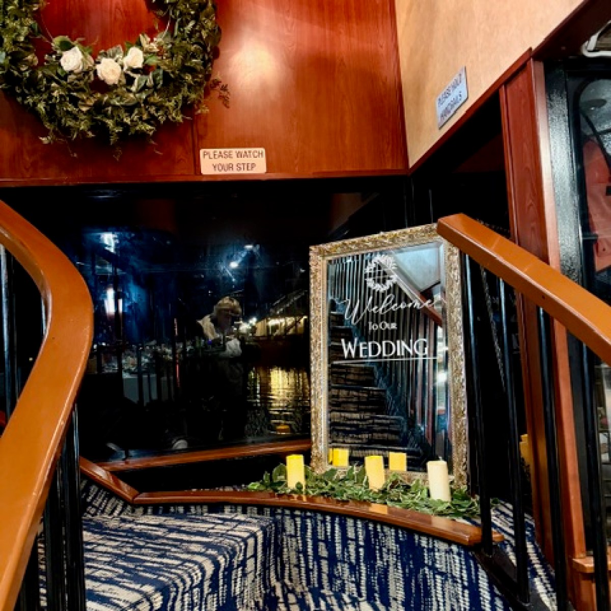 Wedding welcome sign on stairs with candles and wreath above.