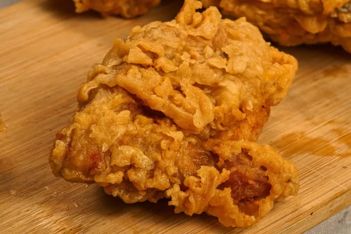 Close-up of crispy fried chicken piece on a wooden surface.