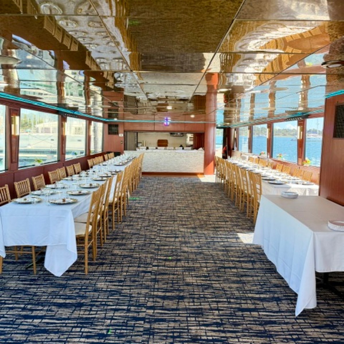 Long dining tables with white cloths set for an event on a boat.