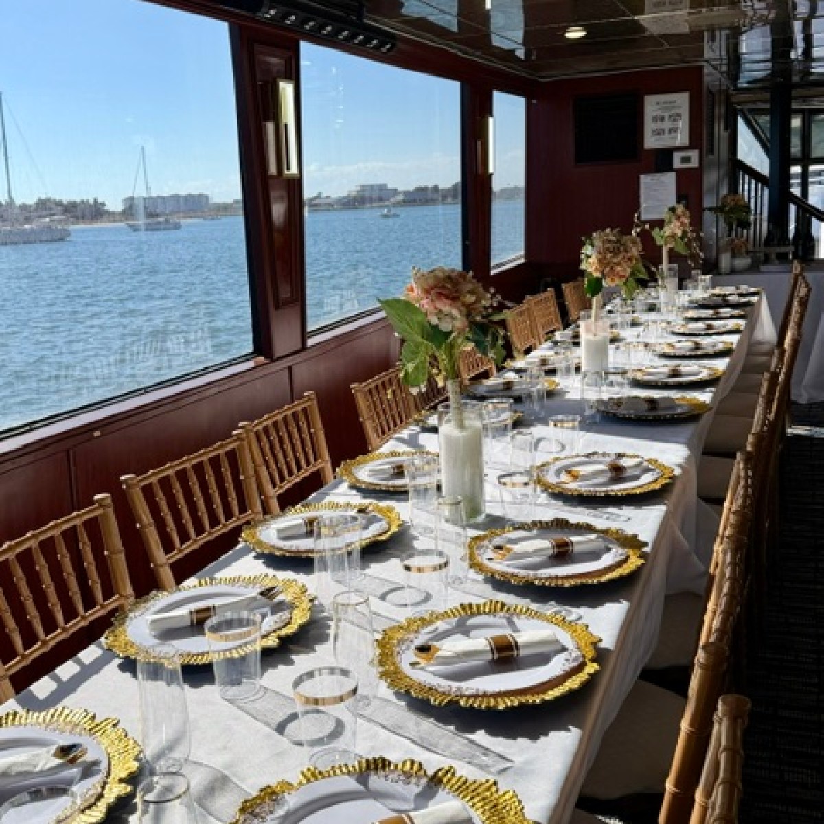 Elegant table setting on a boat with floral centerpieces and gold-accented plates.