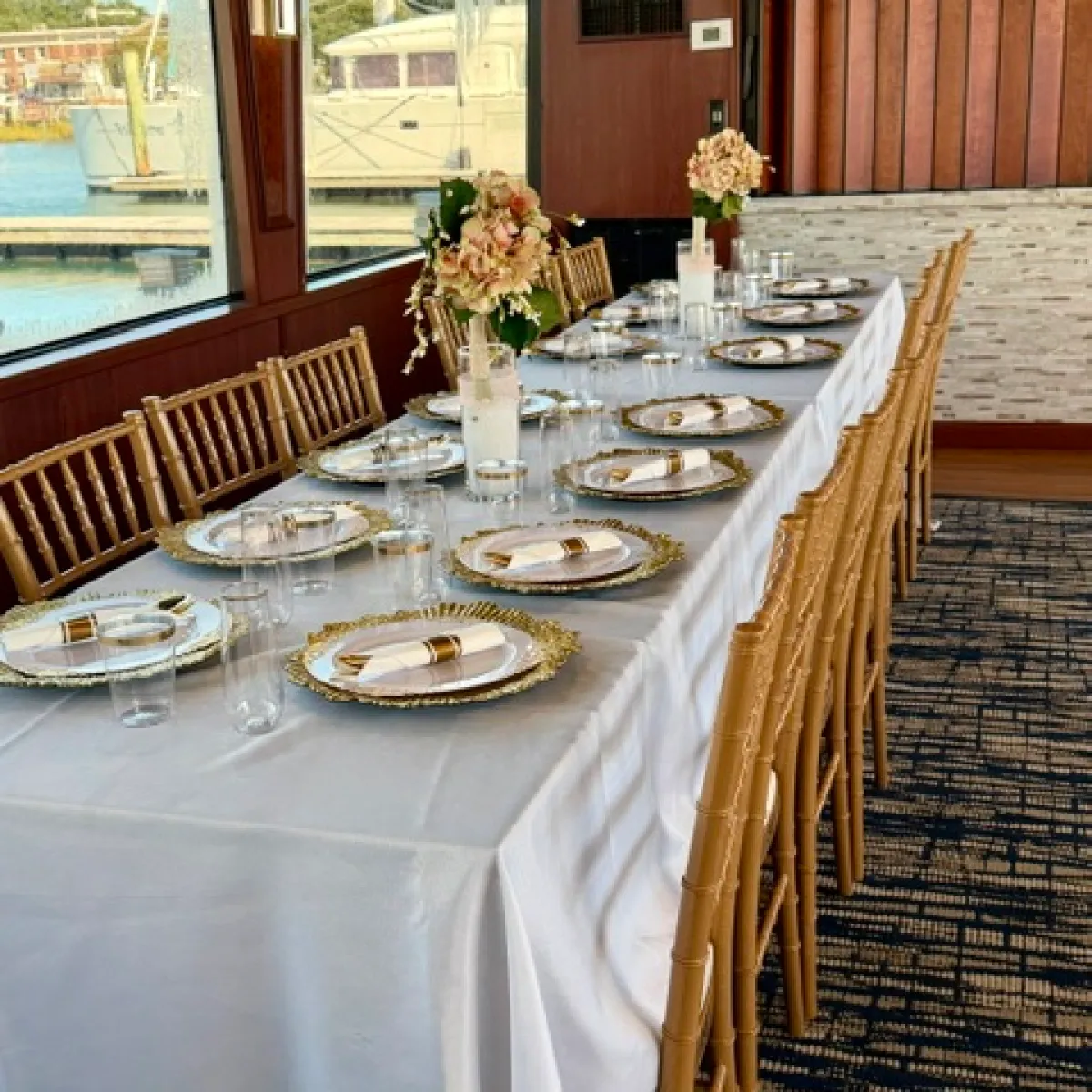 Elegant dining table set with white cloth, floral centerpieces, and gold chairs.
